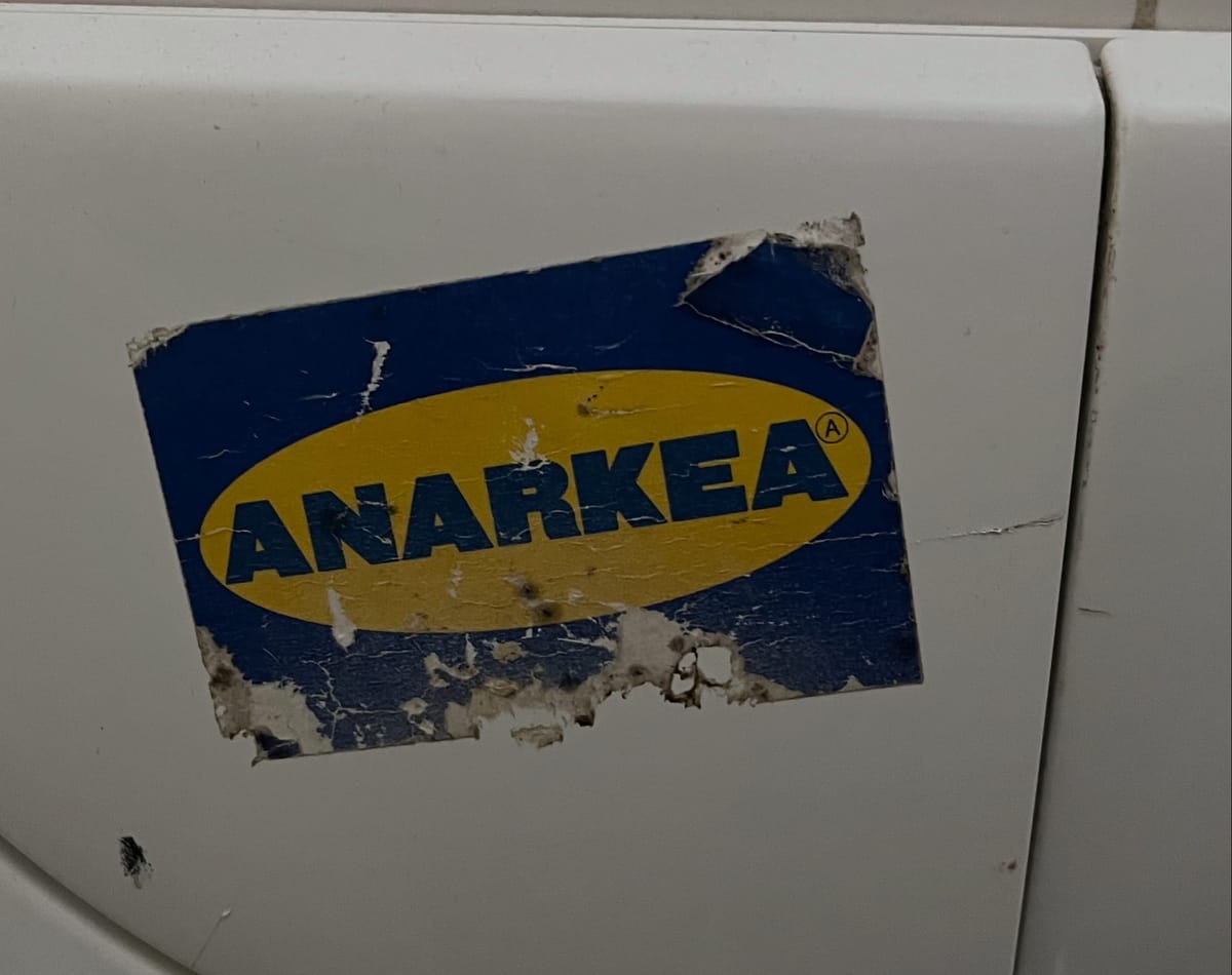 Frayed sticker on toilet wall, in IKEA blue and yellow, reading "ANARKEA"