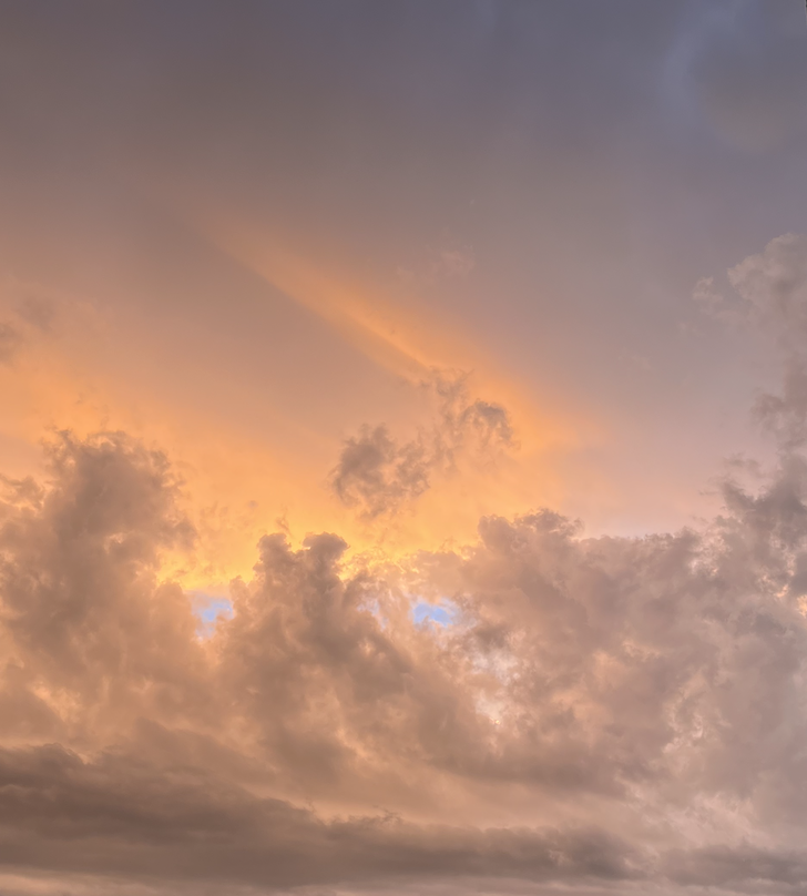 An ominous, post-storm sunset sky over Canberra. Light grey clouds swirling, tiny eyes of blue peeking through beneath pinky-yellow whisps