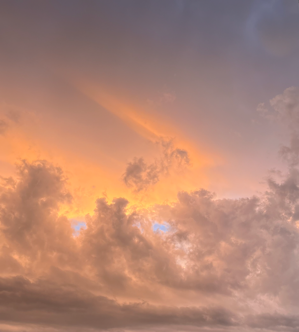 An ominous, post-storm sunset sky over Canberra. Light grey clouds swirling, tiny eyes of blue peeking through beneath pinky-yellow whisps